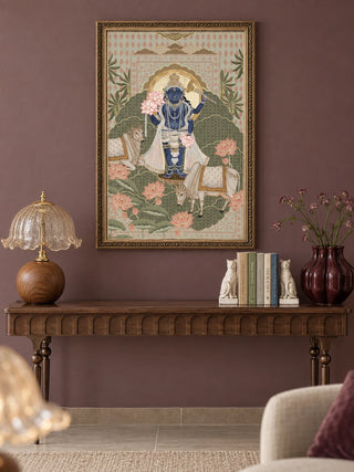 The Shyam Sundar wall art in Sage & Coral, in an ornate gold frame, above a carved wooden console table with a lamp, cat bookends and a plum vase on a mauve wall.
