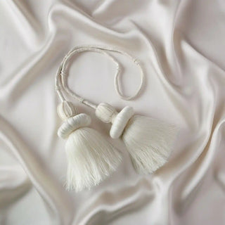 Flat lay of the Silkstone Tassel showing the two ornate, full-bodied ivory tassels and the delicate pearl-like beadwork on a satin background.