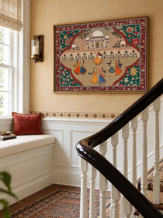 The Sorena wall art in a gold frame, hung on a staircase landing above a cushioned window seat with a rust velvet pillow.