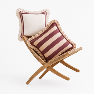 The Spellbound & Cinnamon cushion set styled on a woven rattan bench, showing an ivory cushion with a burgundy border stripe and ruffled edge, and a wide burgundy-and-tan stripe cushion with a ruffled edge.