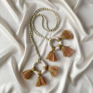 Flat lay of the Springhaven Macrame Tassel showing the woven rings and the pink and green two-tone yarn tassels on a satin background.