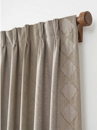 A detailed close-up showing the tailored pinch-pleat header and embroidered diamond ogee border of the Storah curtain on a walnut wood rod