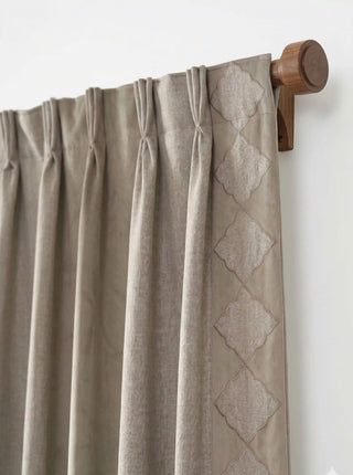 A detailed close-up showing the tailored pinch-pleat header and embroidered diamond ogee border of the Storah curtain on a walnut wood rod