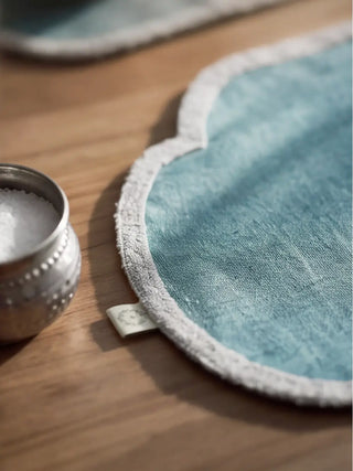 A close-up of the Sufra table mat in Powder Blue showing its scalloped ivory trim and woven brand label.