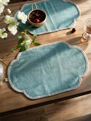 Two Sufra table mats in Powder Blue on a wooden table, styled with a gold bowl of cherries and a glass of wine.