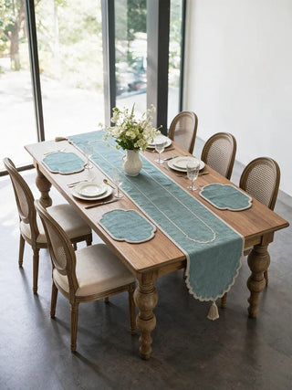 The Sufra table runner and four matching mats in Powder Blue laid on a wooden dining table with white plates, glassware and fresh florals