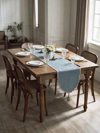The Sufra table runner in Powder Blue styled on a wooden dining table with white plates, crystal glassware and fresh florals.