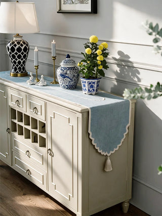 The Sufra table runner in Powder Blue draped over a cream sideboard, styled with ceramic ginger jars, brass candlesticks and a potted plant.