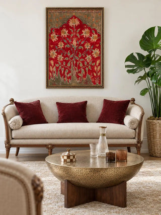 The Sultana wall art in a gilded frame above a carved cream sofa with crimson velvet cushions and a hammered brass coffee table, beside a monstera.