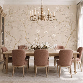 Sunset Serenade chinoiserie wallpaper in Blush Beige behind a wooden dining table with a brass chandelier.