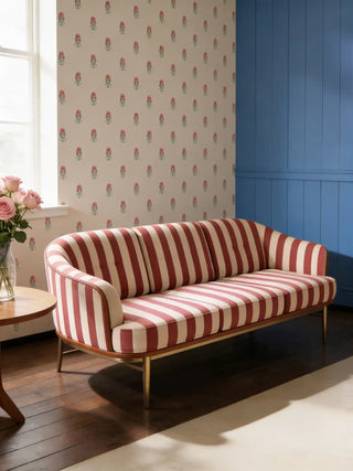 A luxury modern sofa upholstered in Surkh red and cream striped fabric against a floral wallpaper and blue wall.