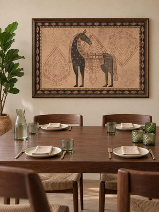The Swarna Ashwa embroidered wall art in a dark carved gilt frame above a walnut dining table with olive glassware and linen napkins