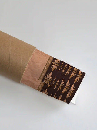 The Swarna Ashwa wall art print partly unrolled from its shipping tube, showing a peach panel and a dark brown border of copper floral rosettes.