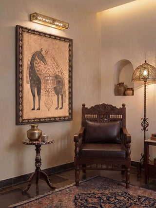 The Swarna Ashwa print styled inside a dark frame under a brass picture light, completing a regal Indian-style reading corner with a leather chair.