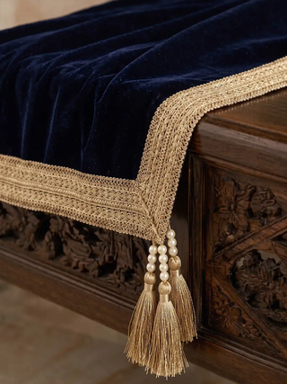 A close-up of the Syahi throw's navy velvet corner, wide gold trim, and pearl-capped gold tassels.