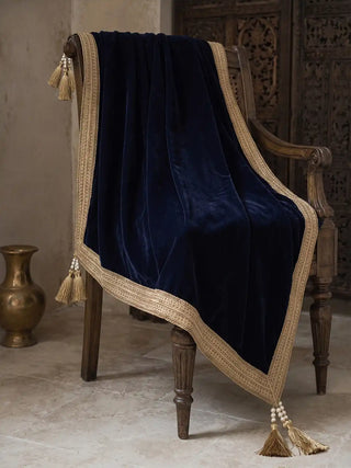 The Syahi navy velvet throw draped over a carved armchair beside a brass vase.