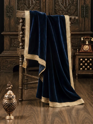 The Syahi navy velvet throw draped over a carved wood chair against a dark panelled backdrop.