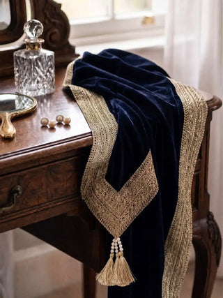 Syahi navy velvet throw over an antique vanity, gold trim and pearl-capped tassels beside perfume bottles