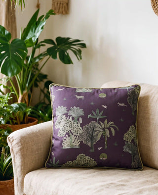 The Taal Dori cushion cover in Aubergine, view-livingroom styled on a linen armchair beside potted palms and monstera.