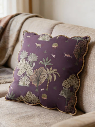 A luxury Taal Scallop cushion cover in dusty mauve with a gold rope-piped wavy edge on a beige upholstered sofa.