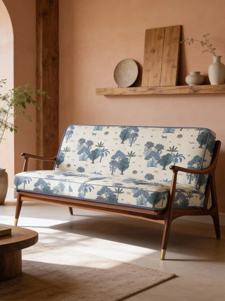 A modern wooden sofa upholstered in Taal ivory fabric featuring a teal tropical landscape with trees and deer.