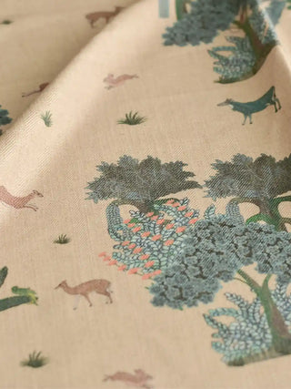 A close-up of the Taal upholstery fabric in Cream & Blue on an armchair, showing trees, palms, and scattered wildlife.