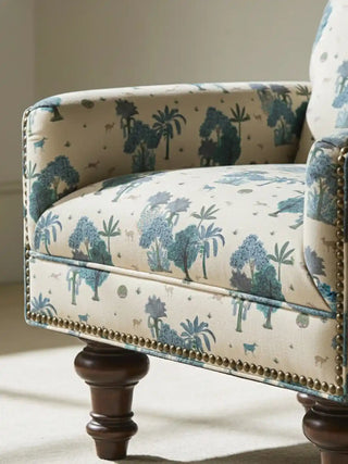 Close up of a luxury armchair upholstered in Taal fabric, showcasing the brass nailhead trim and detailed tropical motifs.