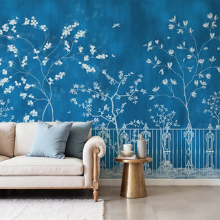 Living room with a blue wallpaper featuring white floral and branch designs, beige sofa, and gold side table.