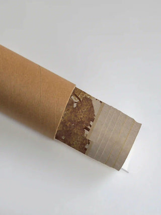 The Forest Nest embroidered wall art partly unrolled from its shipping tube, showing the sepia tree canopy beside a plain ivory border.