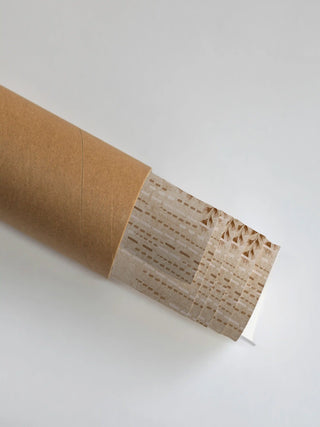 The Secret Garden embroidered wall art partially unrolled from its kraft paper shipping tube, showing the dashed willow fronds in Blush & Bronze.