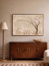 The Secret Garden wall art print in a thin wood frame above a burled wood sideboard with a wooden bowl, beside a beaded floor lamp and bouclé chair.