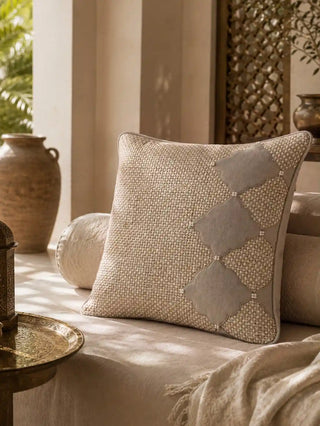 The Sirocco cushion cover with woven jute and velvet diamond detail resting on a sunlit daybed beside a brass tray