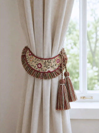 The Thiya crewelwork curtain tieback beautifully gathering a light beige linen drape next to a bright window.