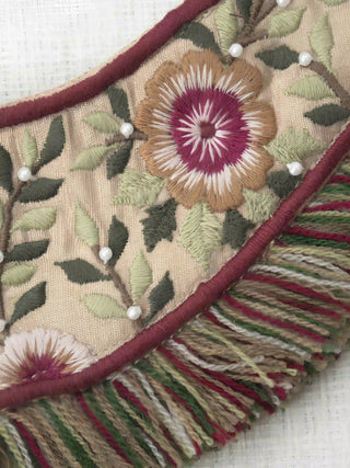 A high-resolution close-up of the hand-stitched crimson floral motifs, sage leaves, and seed pearls on the Thiya curtain tieback.