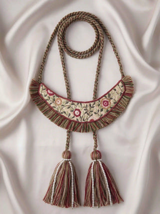 A flat lay view of the Thiya curtain tieback against satin fabric, showcasing the full layout of the crescent panel and corded design.