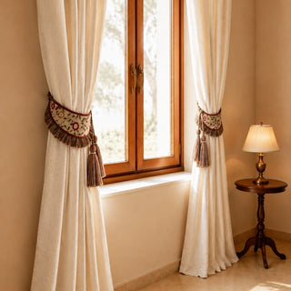 Ivory linen curtains cinched with Thiya hand-embroidered floral tiebacks near a sunlit wooden window