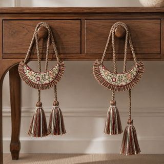 Pair of Thiya embroidered floral tiebacks with beaded tassels hanging from drawer knobs on a wooden console table