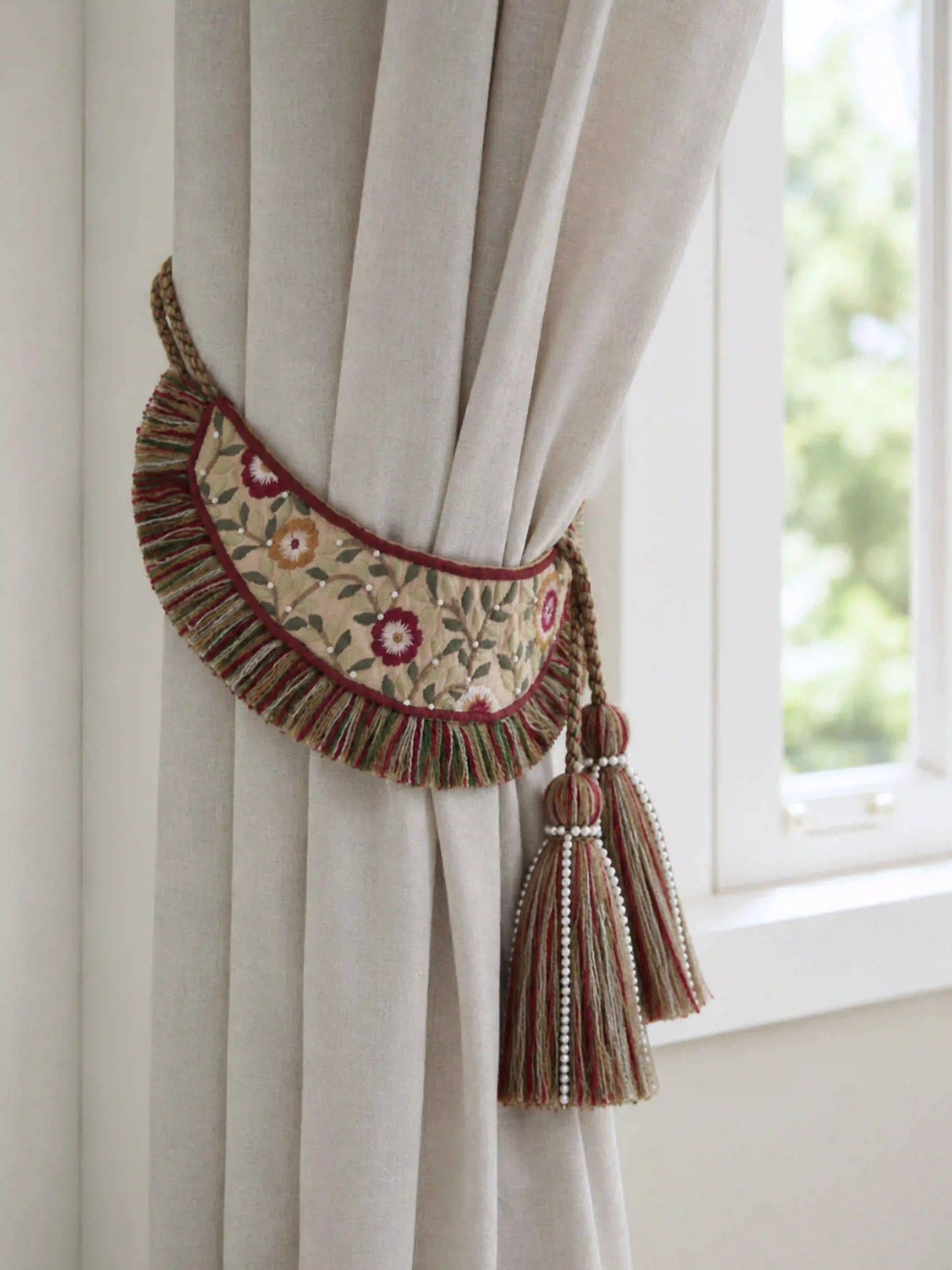 Embroidered curtain tieback with crewel florals and pearl tassels holding a beige linen drape