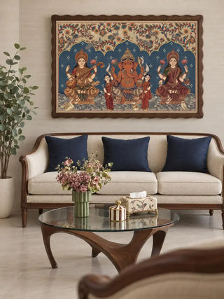 The Trideva Mangalam wall art in a wavy dark wood frame above a cream sofa with navy cushions, a glass coffee table and a potted tree.