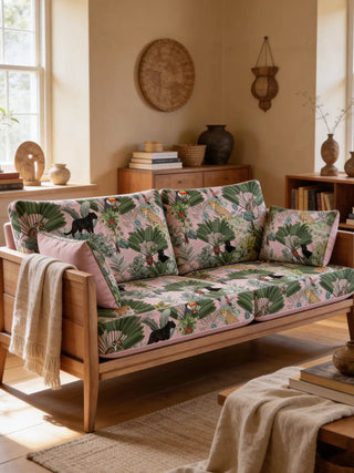 A modern wooden sofa upholstered in Tropical Tales fabric featuring tigers, panthers, and lush green leaves on pink.