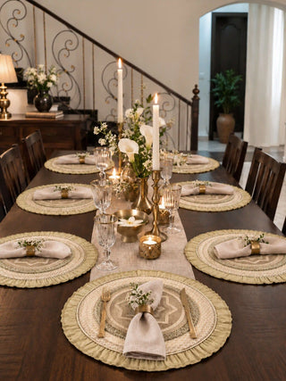 Utsavi round table mats with gold ruffled edges set at each place on a dark wood dining table with linen napkins, brass candlesticks and white calla lilies