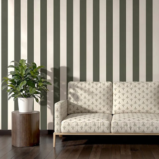 Vanya upholstery fabric in olive ivory on a two-seater sofa with a light wood frame, set against olive striped walls in a living room.