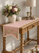 The Veloura table runner in Dusty Rose & Ecru on a carved wooden console table with barley-twist legs, styled with flowers and brass accents.