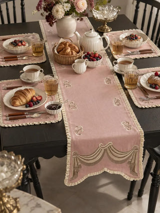 The Veloura table runner in Dusty Rose & Ecru down the centre of a dark dining table laid for breakfast with matching placemats.