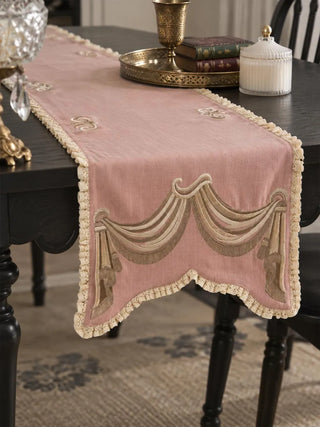 A close-up of the Veloura table runner in Dusty Rose & Ecru showing the draped swag and tassel motif and ruffled lace trim.