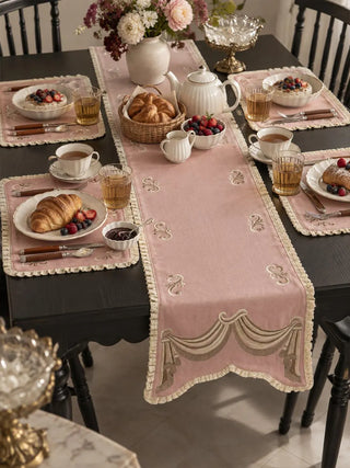 The Veloura table runner in Dusty Rose & Ecru down the centre of a dark dining table laid for breakfast with matching placemats.