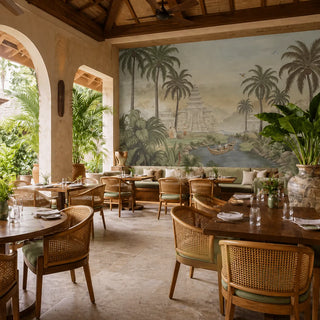 A vintage Chinoiserie tropical landscape mural in antique sage tones behind a wooden dining table and rattan chairs. view-restaurants