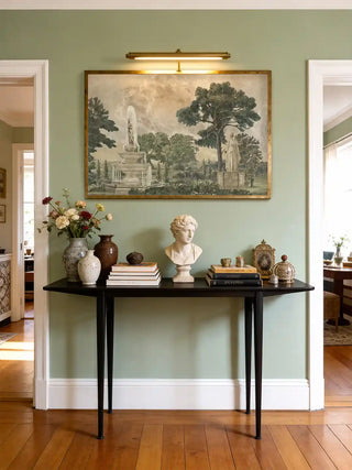 Vintage European Landscape wall art in sage green framed in gold above a black console table with a marble bust, ceramic vases and flowers in a sage painted entryway