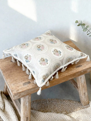 A luxury Vintage Medallion floral cushion in cream jacquard featuring rose bouquet medallions and ivory tassels on a wooden bench.
