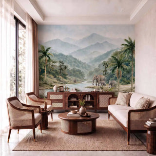 Wayanad Wilderness wall mural covering the full accent wall of a contemporary Indian living room with walnut and rattan armchairs, cream sofa, cane-front sideboard, round walnut coffee table, and jute rug in natural light